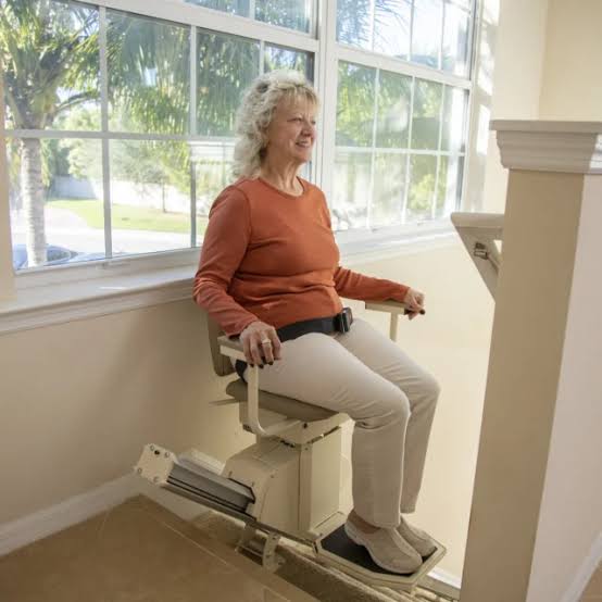 Woman seated comfortably on the Harmar SL600HD Pinnacle heavy-duty stairlift at the top of bright stairs